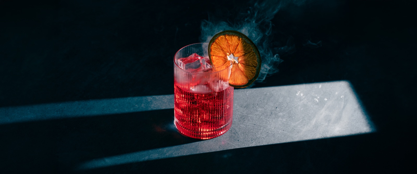 Wide composition of an iced red cocktail with smoke and directional light